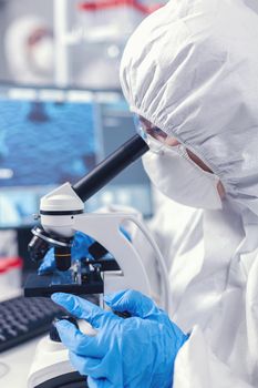 Medical scientist analysing sample on glass slide looking through microscope. Chemist researcher during global pandemic with covid-19 checking sample in biochemistry lab