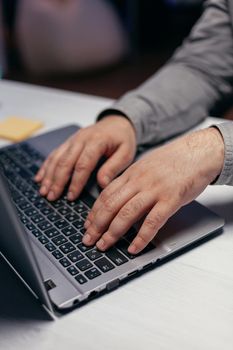 Businessman doing multitasking in dark office. Close up of male hands typing on laptop keyboard in office. Business, working from home, studying online concept