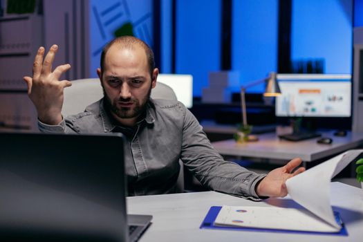 Entrepreneur trying to understand project sitting at his deks in empty office. Confused businessman while doing overtime to finish a big project for company.