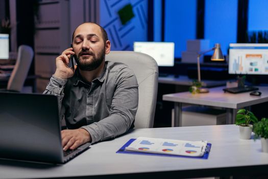 Executive businessman using mobile phone talking about deadline. Manager having a business conversation using smartphone while working overtime at the office.