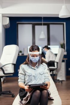 Businesswoman thinking about financial strategy using tablet pc wearing face mask against covid19. Multiethnic business team working respecting social distance during global pandemic with covid-19.