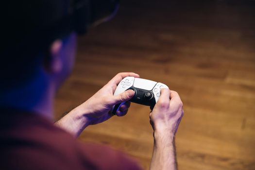 Closeup of man's hands playing video games on gaming console in front of TV widescreen. Man play with dual sense controller. Colorful lights