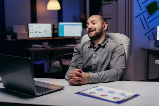 Financial specialist discussing about statistics during online call using laptop and wireless headphones. Businessman in the course of an important video conference while doing overtime at the office.