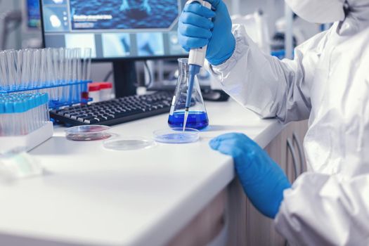 Medicine scientist pouring liquid on petri dish working in lab with micropipette. Chemist in modern laboratory doing research using dispenser during global epidemic with covid-19.