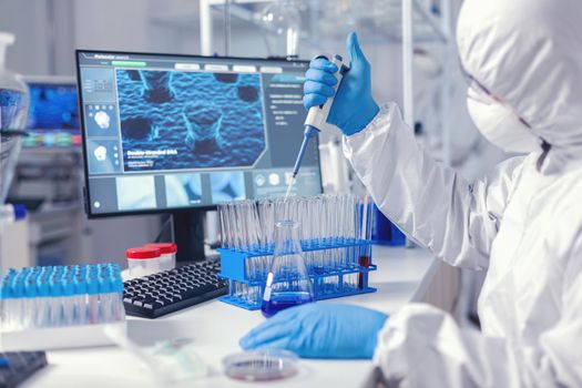 Healthcare researcher in ppe suit working with micro pipette in time of coronavirus. Chemist in modern laboratory doing research using dispenser during global epidemic with covid-19.