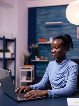 African business woman working on laptop trying to finish a deadline for work from home office late at night. Black entrepreneur sitting in personal workplace writing on keyboard.