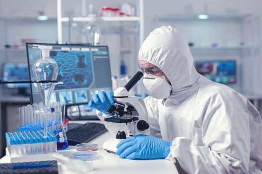 Scientist changing microscope lenses in time of coronavirus experiment dressed in ppe suit. Virolog in coverall during coronavirus outbreak conducting healthcare scientific analysis.