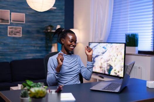 Cheerful darked skinned woman in the course of work from home in living room using laptop. Black woman enjoy e-learning process, easy application usage overtime.