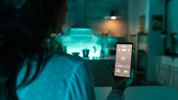 Woman using automation phone app to change light color remotely. Person in apartment holding telephone with touchscreen and app for lights.