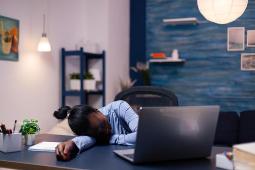 African business woman sleeps during late night hourse in the course of deadline working from home. Busy employee using modern technology network wireless doing overtime sleeping on table.