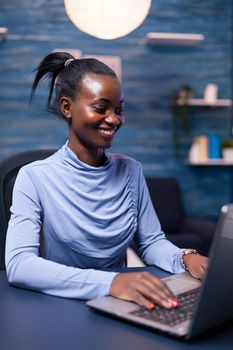 Cheerful african woman speaking in the course of video call looking at laptop webcam in home office. Black freelancer working with remotely team chatting virtual online conference.