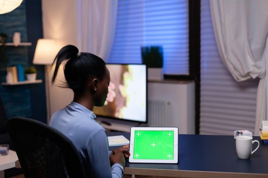 African freelance woman enjoying working from home looking at tablet pc with copy space availablesitting at desk. Using mockup chroma key display computer.