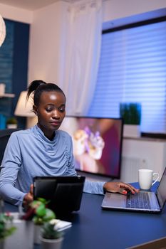 African freelancer using tablet pc working from home working late at night. Busy focused employee using modern technology network wireless doing overtime writing.