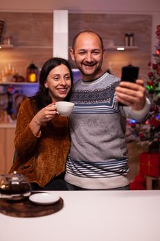 Smiling family taking selfie using smartphone enjoying christmas time standing in xmas kitchen. Happy joyful family celebrating winter holiday season. New year festive season