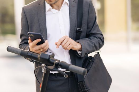 Unrecognizable businessman in suit is coming up to an electric scooter. Phone application for rental scooter. Ecological city transport. Businessman rents electric scooter using mobile phone app.