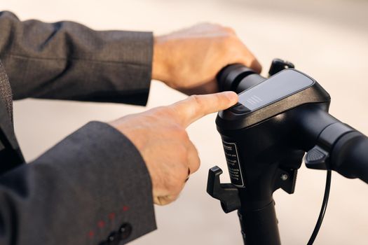 Close up of unrecognizable businessman turns on the electric scooter. Male is pushing start button of modern gadget on street of city. Hands of a young man close-up. Ecological alternative transport.