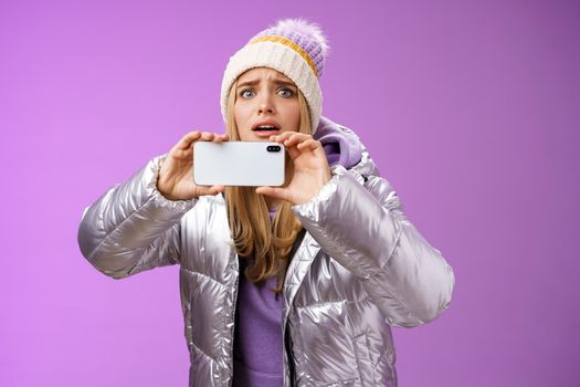 Intense worried blond girl holding mobile phone horizontal recording video capture moment share friends internet blog using smartphone camera shoot photograph standing serious purple background.