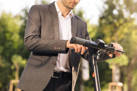 Unrecognizable businessman unlock and riding an electric scooter for a business meeting in the office, office buildings, business man, electric transport, ecological transport.