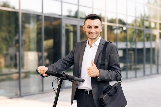 Portrait of caucasian businessman leaning on electric scooter and looking at camera. Stylysh man on vehicle outdoors. Eco-friendly modern urban transport. Ecology and urban lifestyle.
