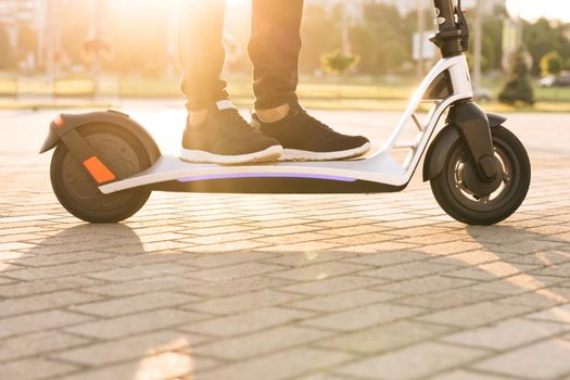 Close up feet man courier food delivery rides the street on electric scooter deliver online order client at sunset. Shot on legs young man in black sneakers ride on electric mobile scooter.