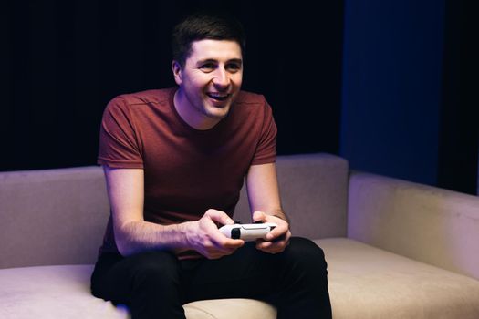 Caucasian guy playing video game and using joystick . Handsome young man enjoying free time alone while sitting on couch in living room.