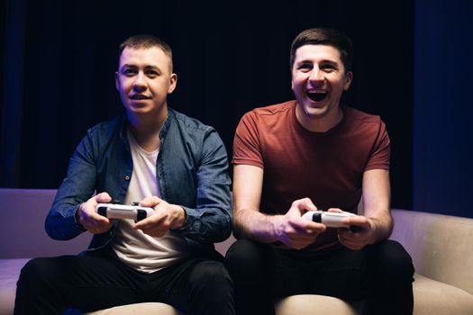 Excited funny young adult men gamers holding controllers playing video game friends winning videogame having fun together celebrating victory at home