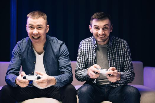 Funny young adult couple men gamers holding controllers playing video game friends winning video game having fun together celebrating victory at home
