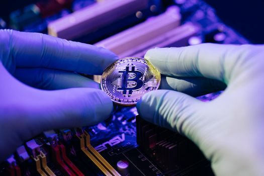 Closeup of Businessman hands hold gold Bitcoin on motherboard background. Cryptocurrency in the fingers. Person shows future currency. Mining, trading.