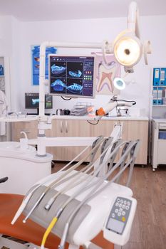 Stomatology dental medical chair with nobody in it equipped with dentistry tools prepared for orthodontic teeth surgery. Professional orthodontist display with tooth radiography images