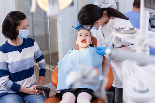 Dentist using modern dental equipment for little girl treatment in clincic. Dentistry specialist during child cavity consultation in stomatology office using modern technology.