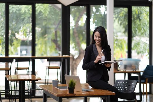 Portrait of beautiful smiling young entrepreneur businesswoman working with laptop computer during taking note on notepad.