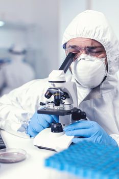 Close up of medical engineer doing research on covid virus wearing ppe. Scientist in protective suit sitting at workplace using modern medical technology during global epidemic.