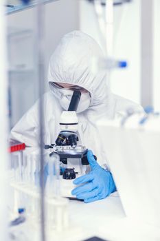 Laboratory engineer conducting experiment for vaccine against coronavirus using microscope. Chemist in coverall examining vaccine evolution using high tech researching diagnosis against covid19 virus