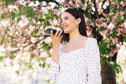 Happy young girl using smart phone voice recognition, dictates thoughts, voice dialing message outdoor talking to mobile assistant. Talking mouth in the speaker of a young woman.