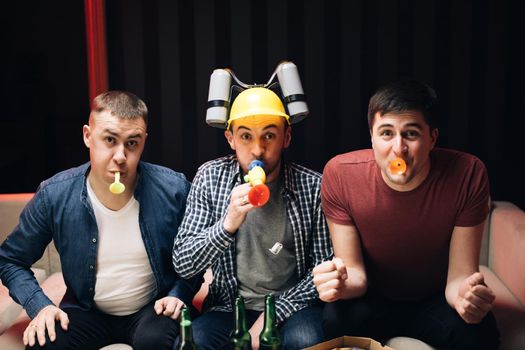 Group of Friends Watches TV in the Home. Their Team Scores the Goal and Wins. Young People Cheer. Three happy male friends resting in the evening at home with beer and cheering up for a goal.