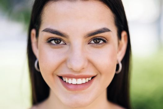 Beautiful face of tender attractive woman staying outside. Attractive young lady with her hair blowing in the wind. Perfect model with creative vivid makeup and pink lipstick on lips. Ethnicity.