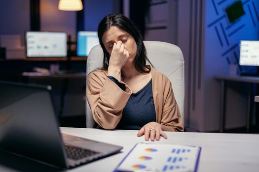 Businesswoman having a migraine in the course of overtime hours for job to work in deadline. Employee falling asleep while working late at night alone in the office for important company project.