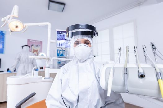 Patient pov of dentist explaining teeth treatment dressed up in covid protective suit. Stomatolog wearing safety gear against coronavirus during heatlhcare check of patient.