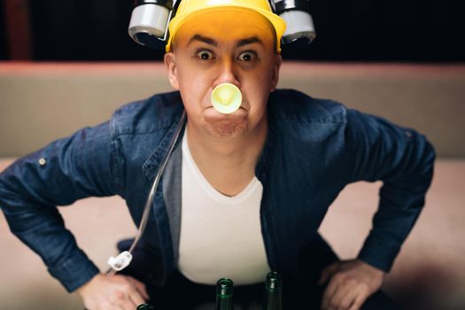 Expressing, screaming and emotion. Man with beer helmet on the head sitting on the sofa and watching football.