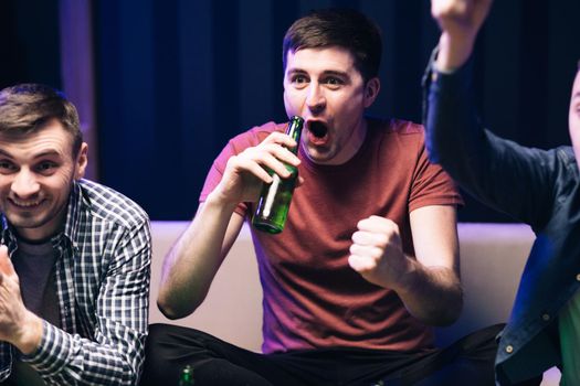 Men watching TV with sport channel late at night and drinking beer. Cheerful happy Caucasian guys cheering for favorite team. Loyal football fans supporting their team.