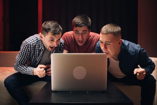 Men watching football in streaming on laptop. Men fans buddies supporters cheering celebrating victory goal score support winning team. Male friends watching online football game match at laptop.