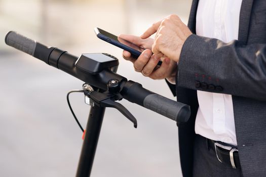 Unrecognizable man using smartphone app. Businessman approaches an electric scooter and using mobile phone app NFC contactless locker on bike bicycle in sharing parking lot. Ecological transportation.