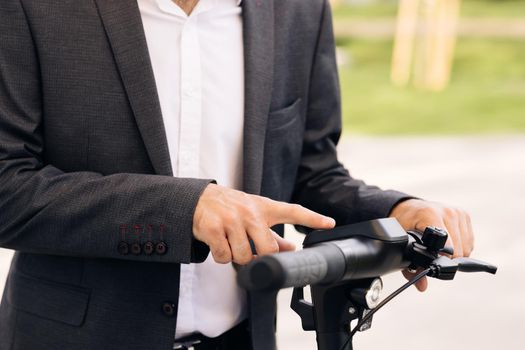 Unrecognizable person turns on the electric scooter. Man activates an electric scooter, a steering wheel close-up. Hands of a young man close-up. A man is holding onto her electric scooter.