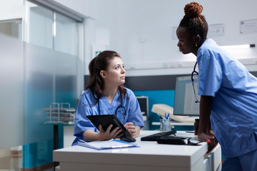 Medical nurse team working at sickness diagonisis discussinng symptoms in hospital office during clinical examination. Multi-ethnic asisstances analyzing pharmaceutical prescription on tablet