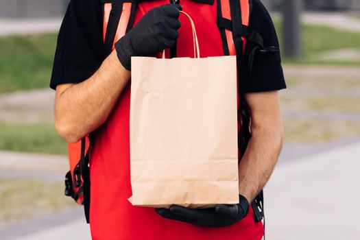 Close up handsome courier man holding paper bag with food at street outdoors worker grocery to house door to door delivery. Online order, fast home delivery.