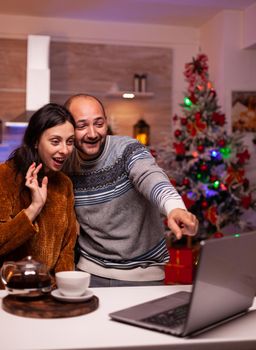 Happy family greeting remote friends during online videocall meeting conference enjoying spending time together in xmas decorated kitchen. Joyful couple celebrating winter season