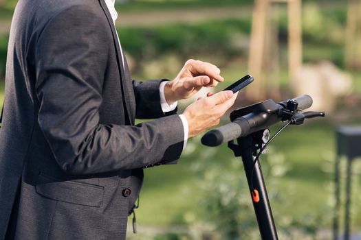 Unrecognizable hands with phone. Tourist taking e-scooter or bicycle. Phone application for rental scooter. Ecological city transport. Businessman rents electric scooter using mobile phone app