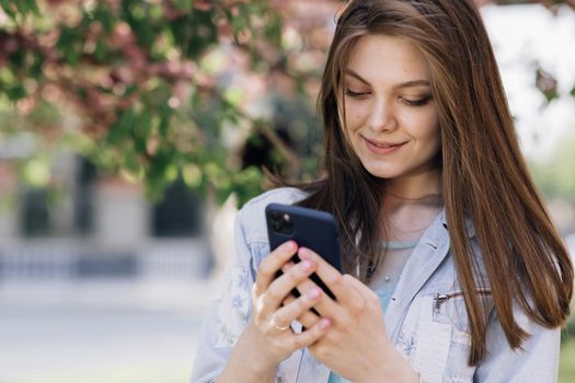 Smiling woman using smartphone. Girl using social media application text messages receive news smiling outdoor. Communication, social networks, online shopping concept. Technology.