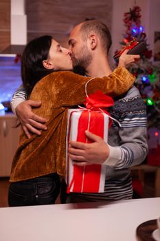 Happy family kissing eatch other after surprising with xmas present with ribbon on it celebrating christmas holiday together in x-mas decorated kitchen. Cheerful joyful couple enjoying winter season