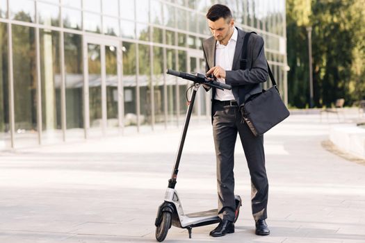 Man uses an electric scooter as a modern means of transportation in the city. A male businessman approaches an electric scooter and using mobile phone app. Ecological transportation.